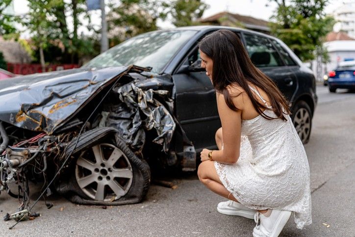 A woman beside a damaged car, reflecting on a car accident scene in Phoenix, AZ