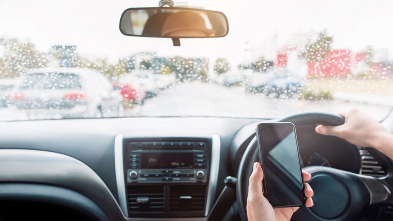 Person driving a car in Phoenix, AZ, holding a phone in one hand, illustrating distracted driving.