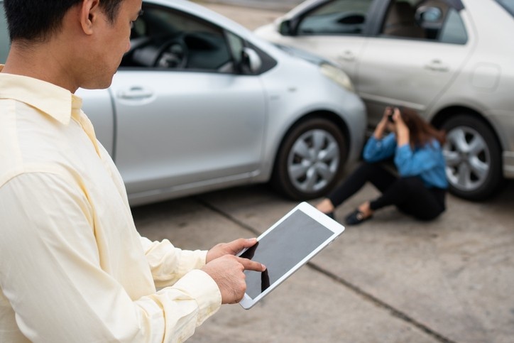 A man with a tablet stands beside a car in Phoenix, AZ, illustrating rideshare accident lawyer services.